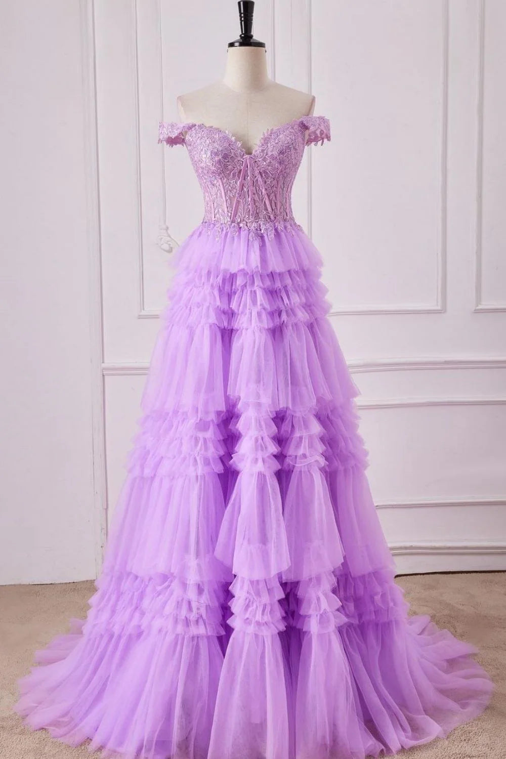 Model wearing a purple A-line off-shoulder prom dress with applique lace and tiered tulle.