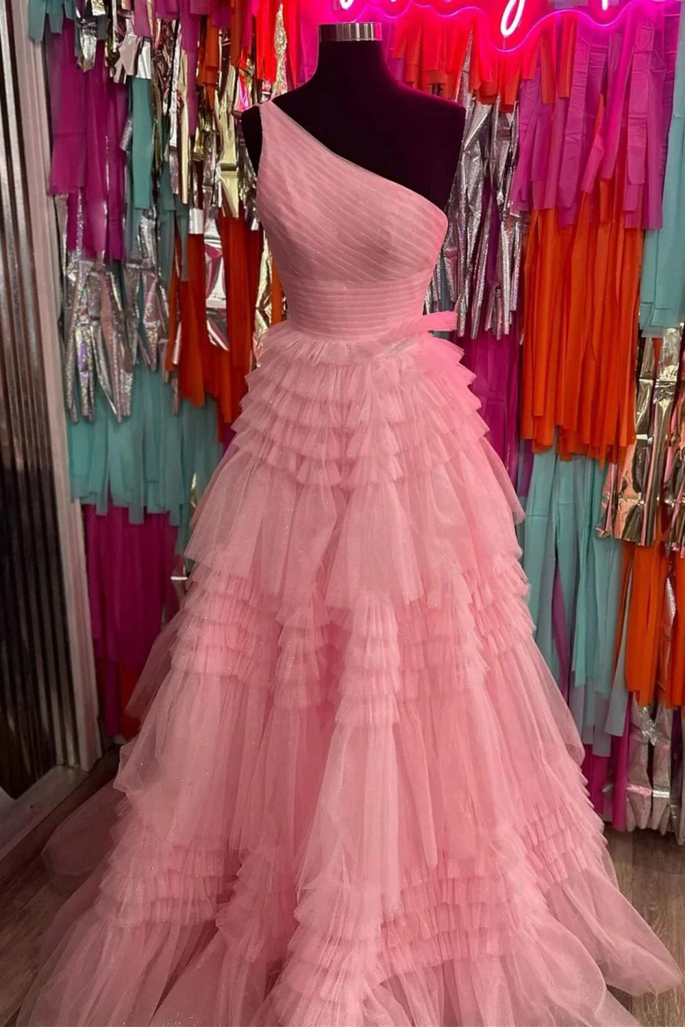 Model wearing an elegant pink A-line one-shoulder pleated tiered ruffle prom dress, full length view.