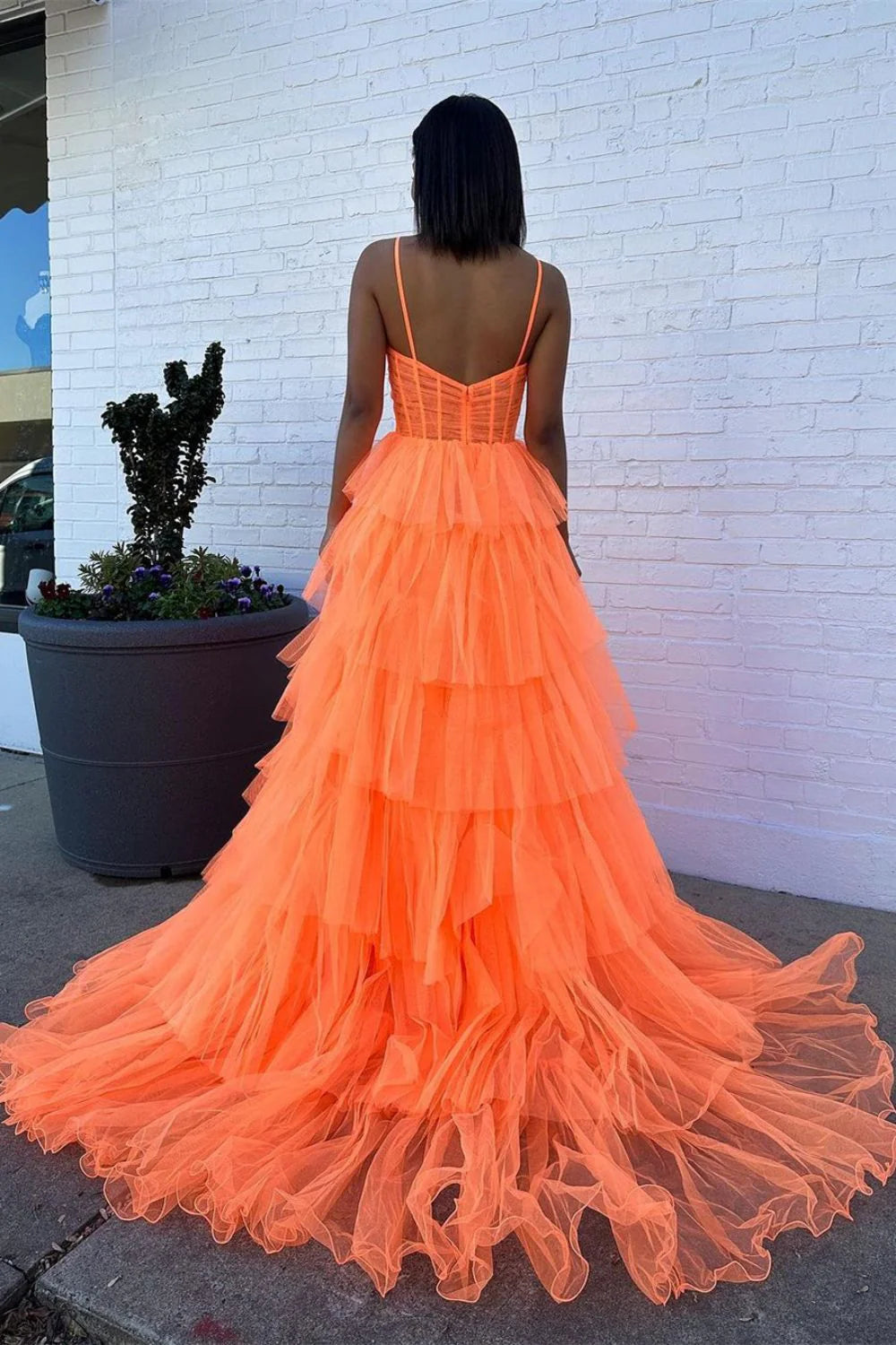 Front view of an orange A-line prom dress featuring spaghetti straps and a tiered ruffled skirt.