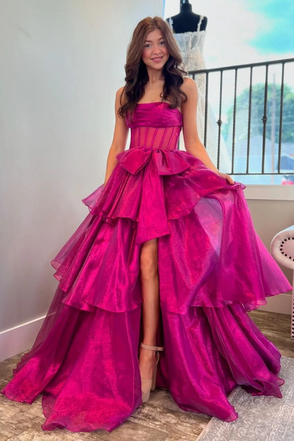 Model wearing a fuchsia A-line strapless prom dress with a bowknot and slit, side view.