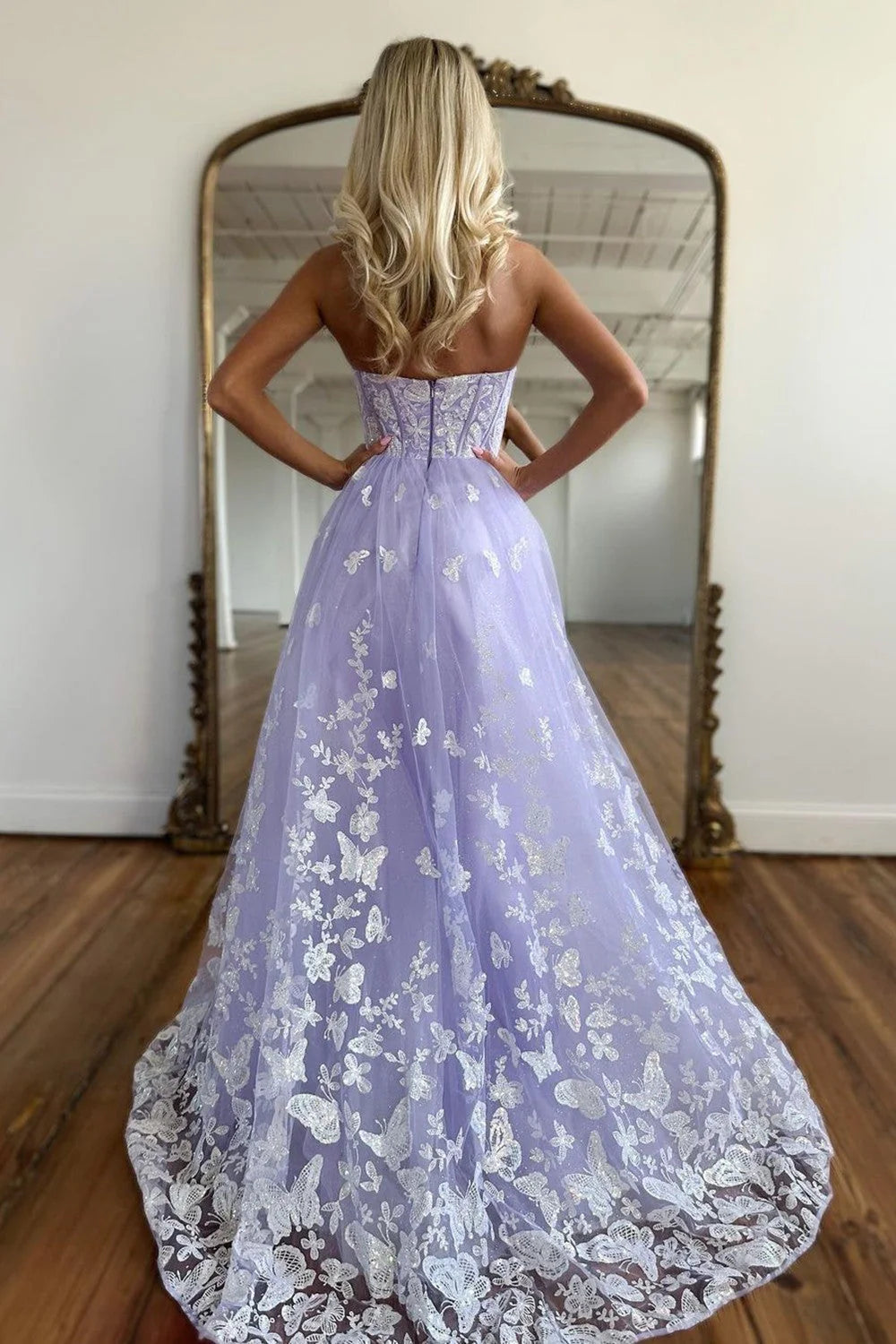 Woman posing in a long lilac A-line prom dress with a sweetheart neckline and intricate appliques.
