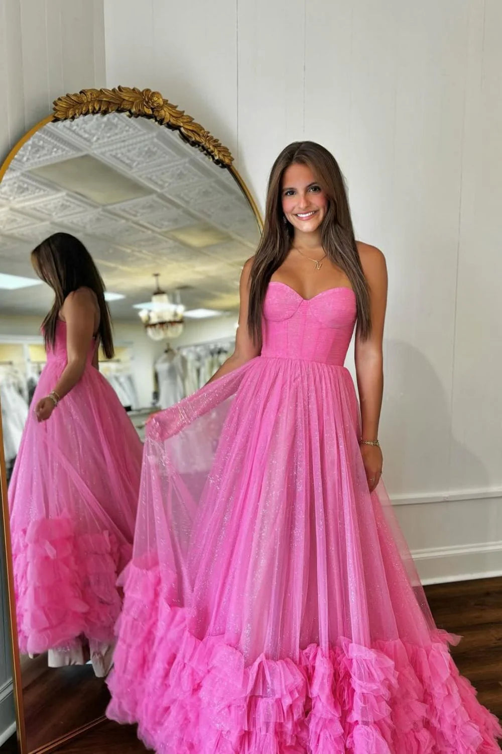 Model wearing a long pink A-line prom dress with sweetheart neckline, ruffle details, and glitter tulle fabric.