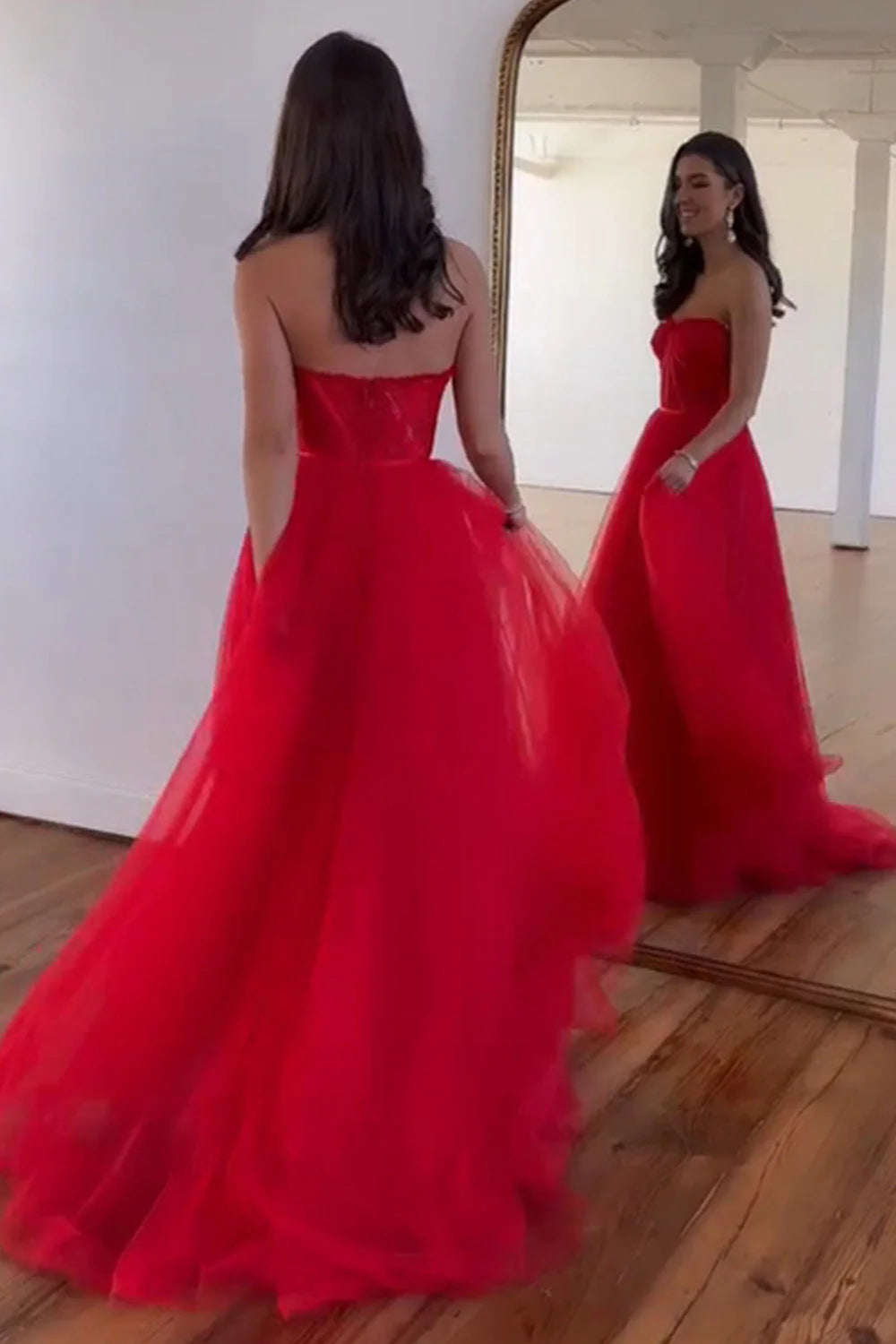 Model wearing a red A-line sweetheart tulle gown, showcasing its flowing floor-length skirt.