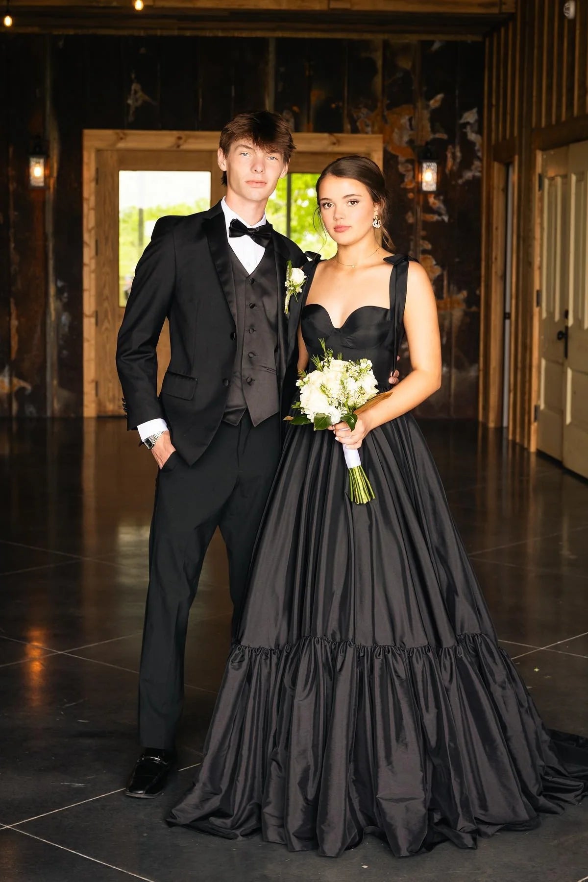 Full length view of an elegant black satin A-line prom dress with tie straps and a tiered skirt.