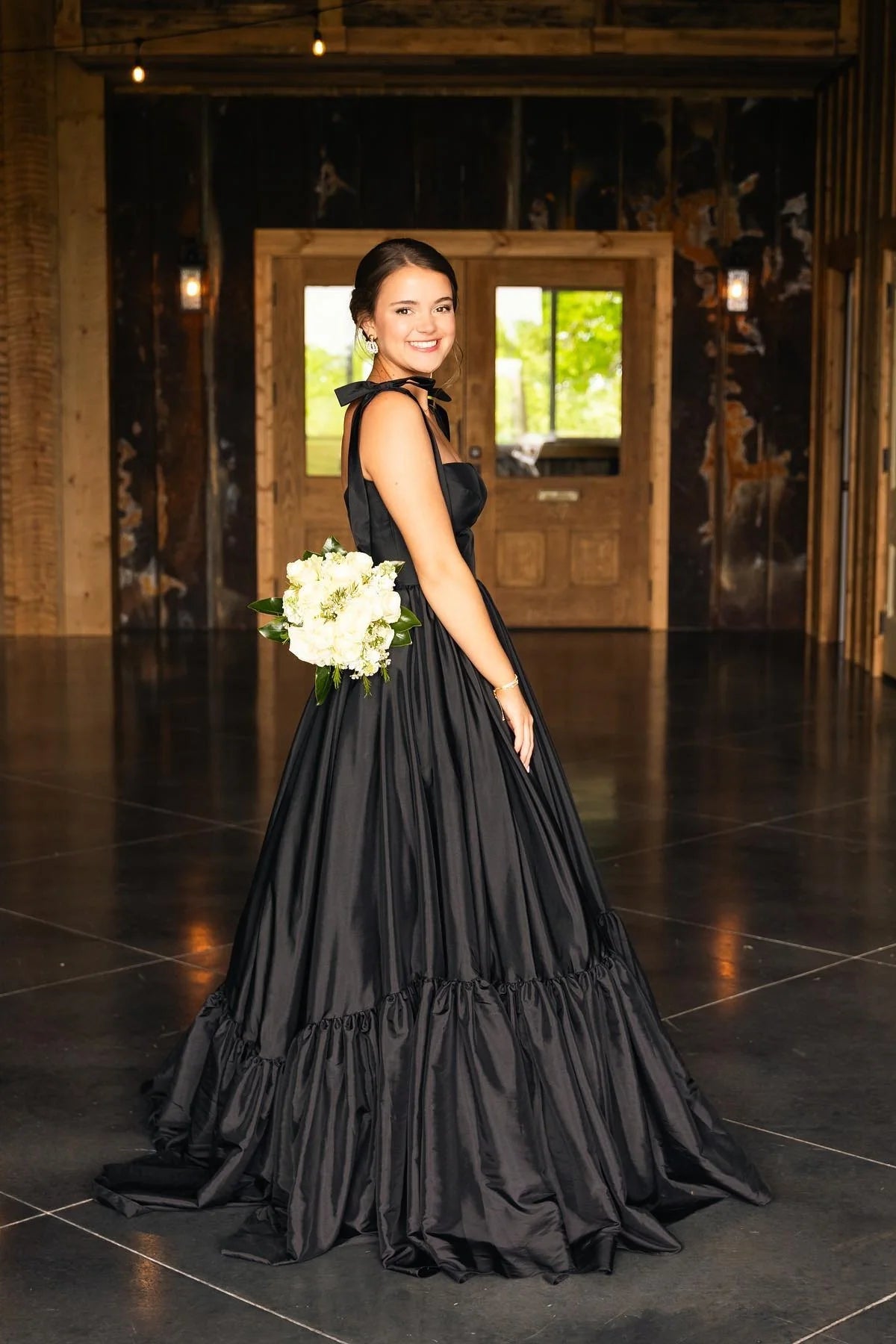 Back view of the black satin A-line prom dress, highlighting the open back and adjustable tie straps.
