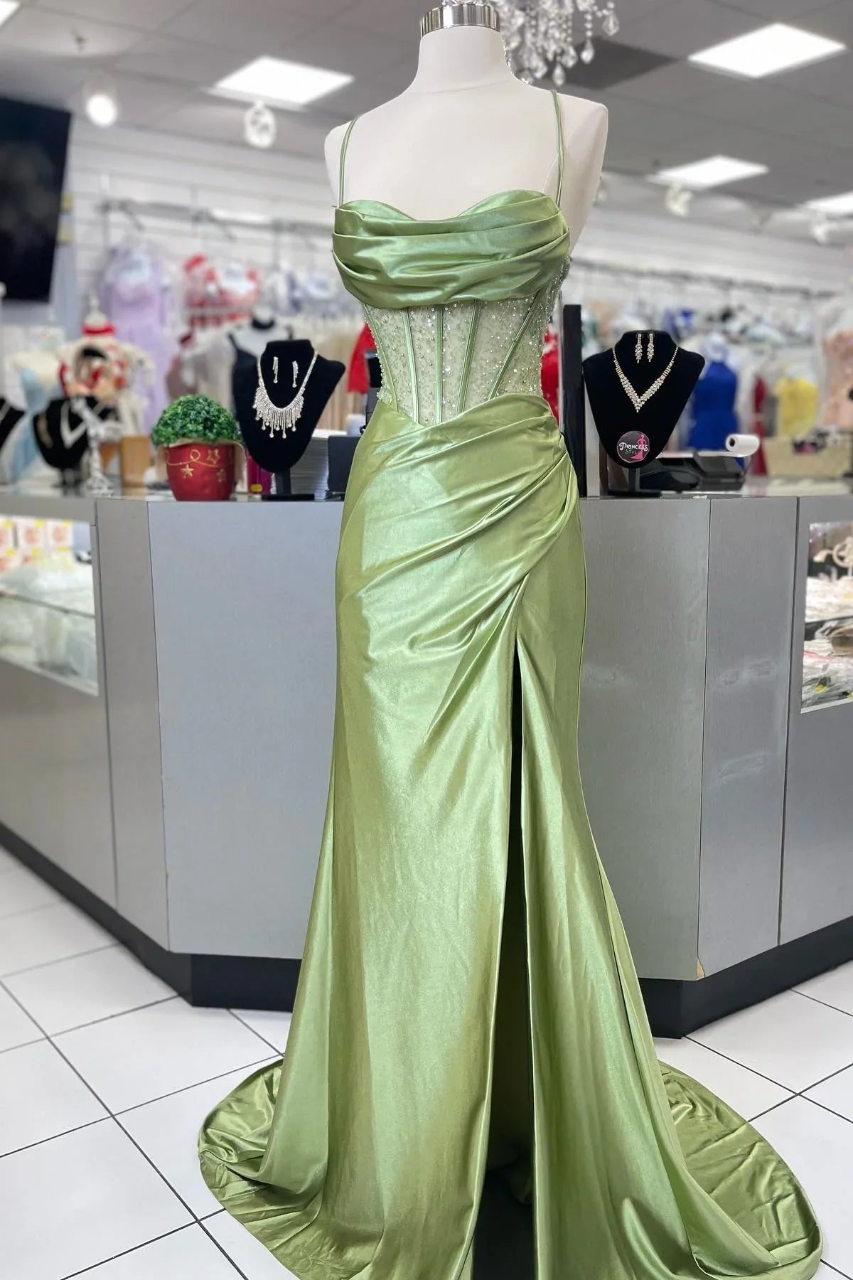 Model wearing a green mermaid prom dress with spaghetti straps and high split.