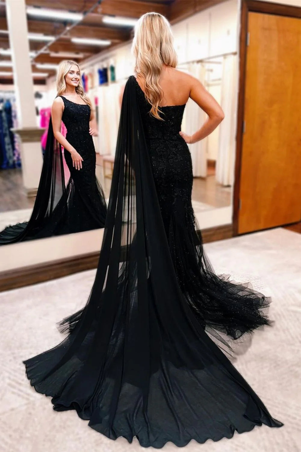 Model wearing a black one-shoulder mermaid gown with intricate beading and a long train.