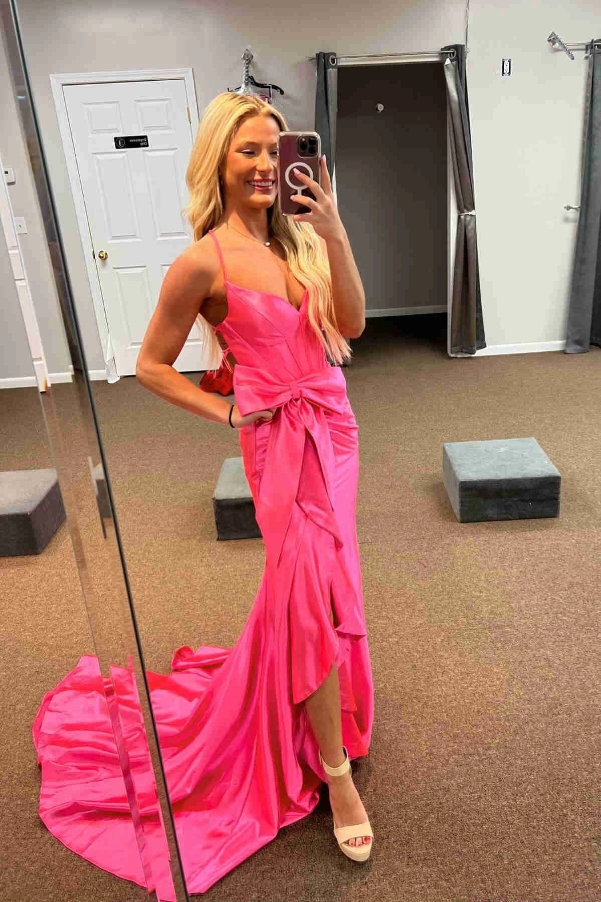 Model wearing a hot pink mermaid prom dress with a large bowknot and high slit.