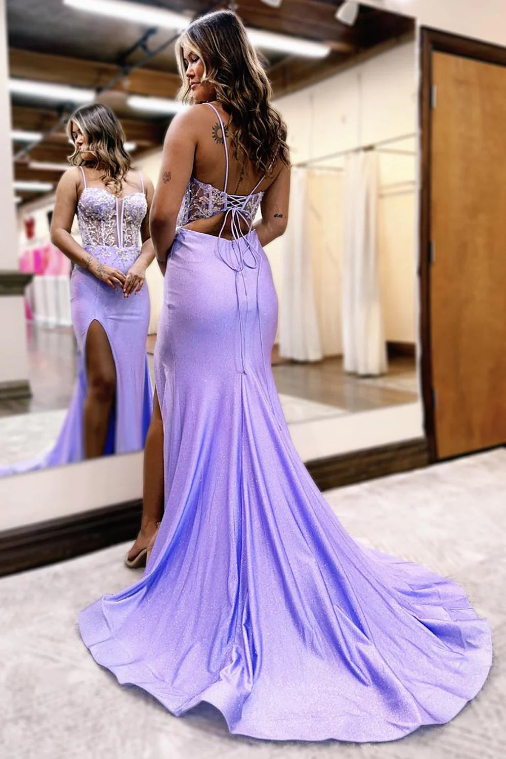 Back view of a woman in a lilac mermaid prom dress with lace-up detail and sweep train.