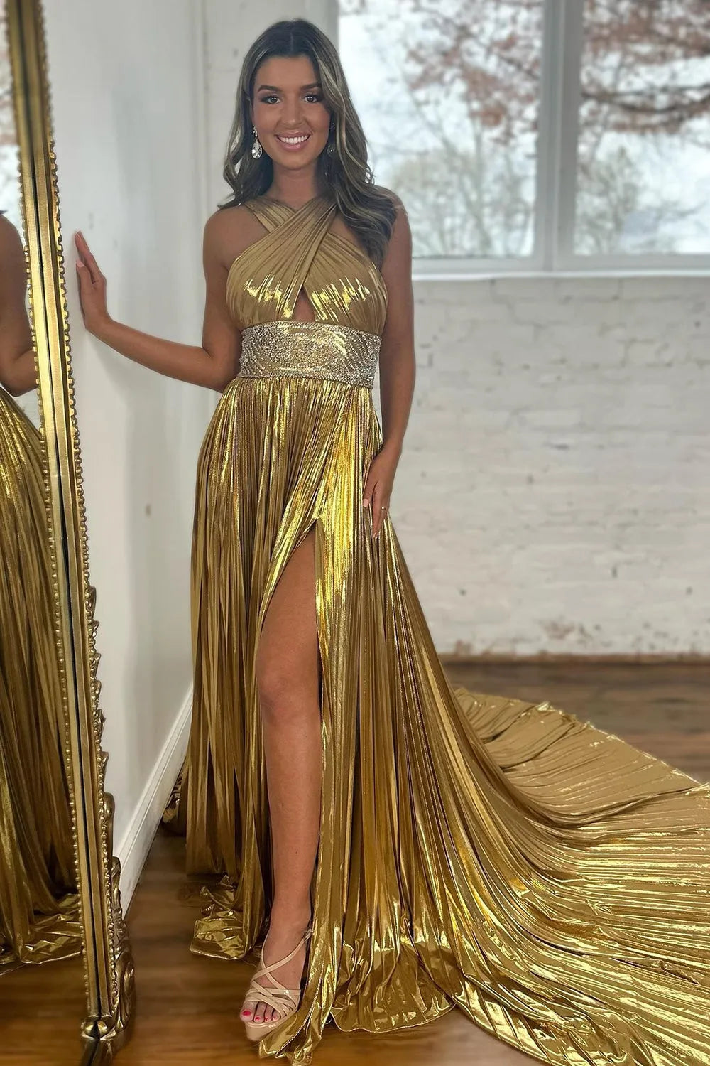 Full view of a shiny gold A-line prom dress with criss-cross straps, keyhole, beading, and a long train.
