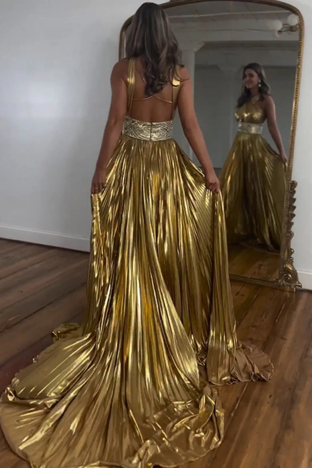 Back view of a shiny gold A-line prom dress showing criss-cross straps, open back, and long train.
