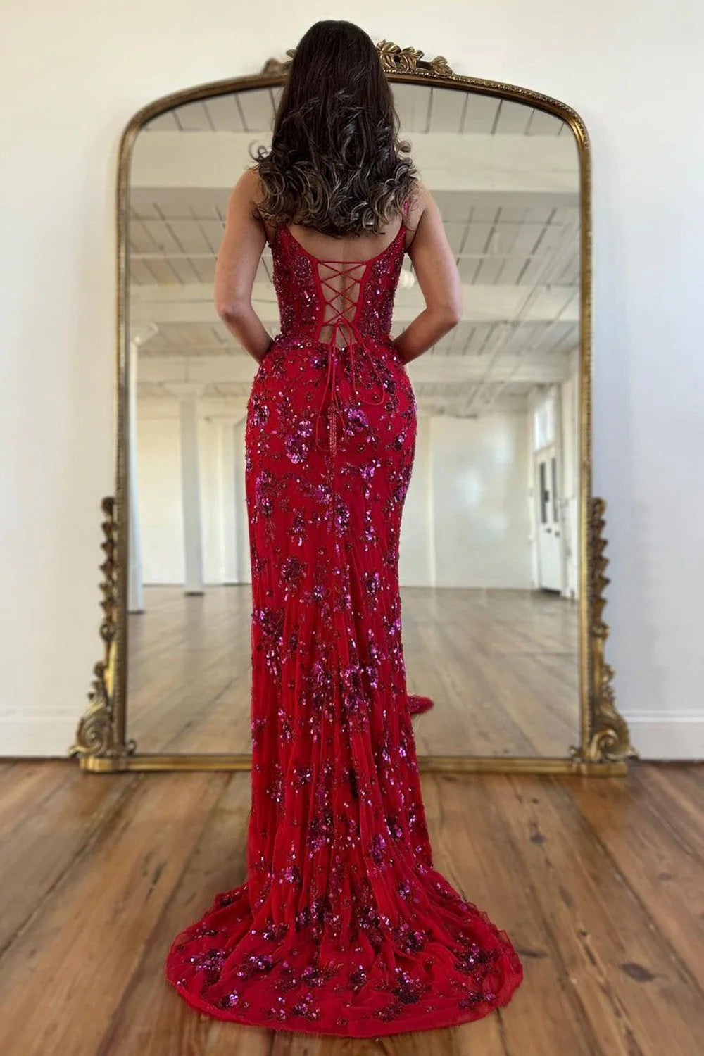Back view of a woman in a red sequined mermaid prom dress with a lace-up corset.