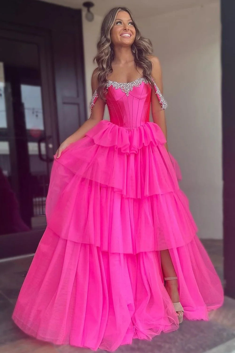 Model wearing a hot pink A-line off-shoulder prom dress with beading and tiered tulle skirt.