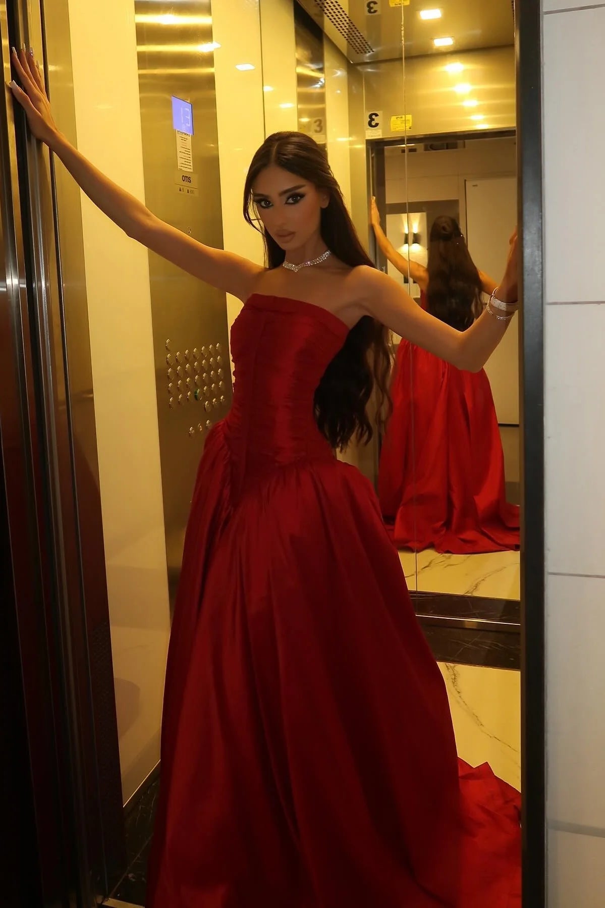 Woman wearing a red A-line strapless pleated long prom dress with a train.