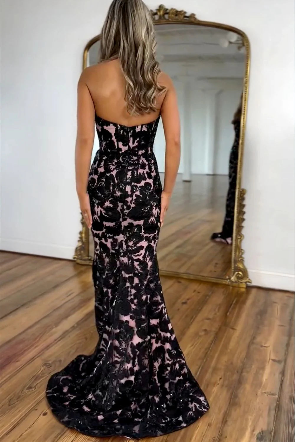 Elegant black mermaid gown with a sweetheart top, detailed appliques, and a flowing train, viewed from the side.