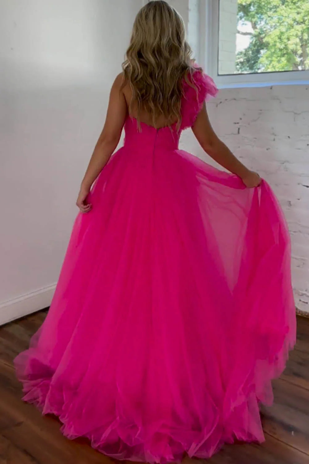 Hot pink A-line one-shoulder pleated tulle prom dress, showing open back and split.