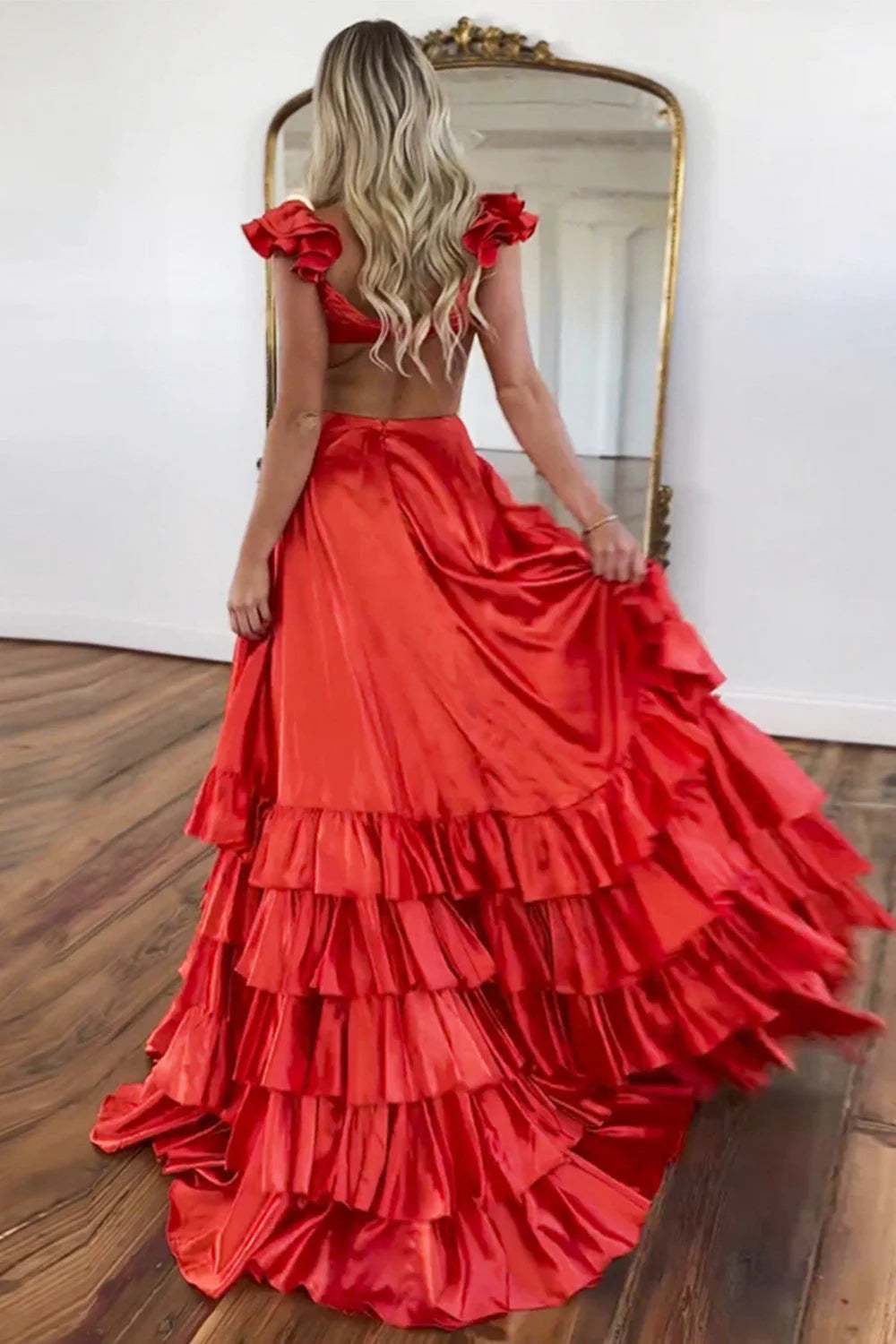 Back view of the coral red A-line prom dress showing open back and tiered satin skirt.